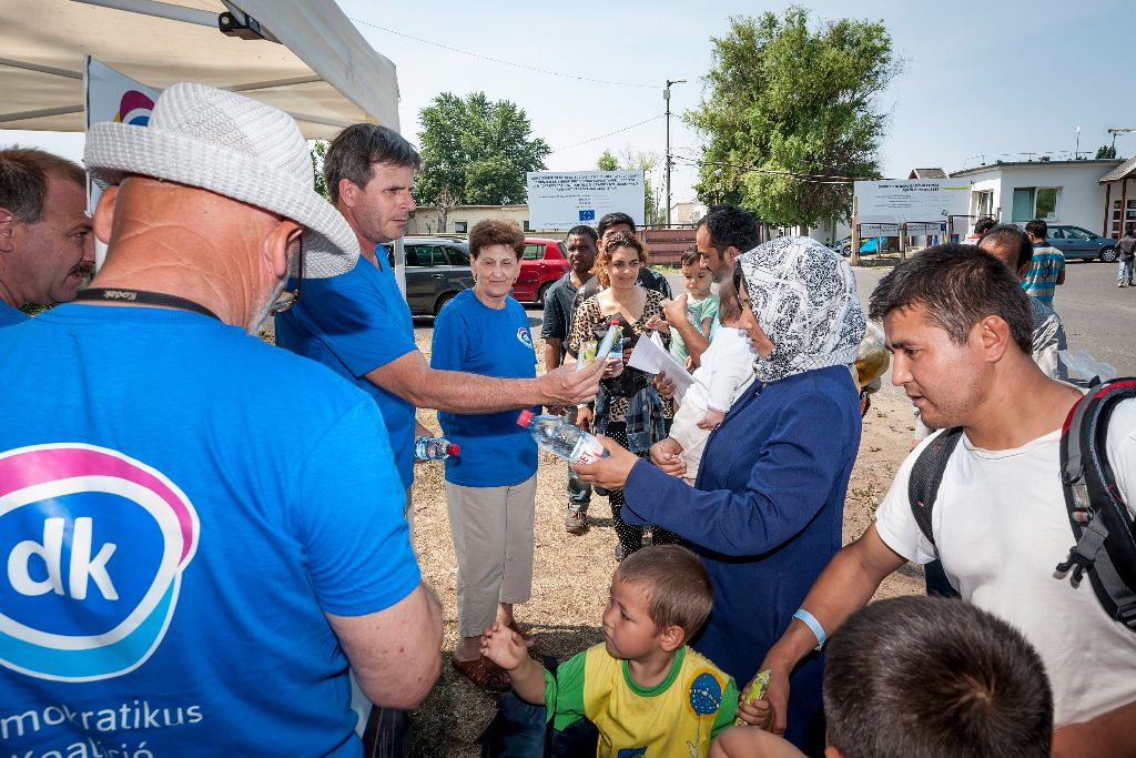 Debrecen, 2015. július 6. Varga Zoltán, a Demokratikus Koalíció (DK) debreceni elnöke (b2) és a párt aktivistái palackozott vizet és müzliszeletet osztanak a Bevándorlási és Állampolgársági Hivatal debreceni befogadó állomásán élõknek a tábor bejáratánál 2015. július 6-án. Az országos tiszti fõorvos július 4-tõl, szombattól július 8-ig, szerda éjfélig a legmagasabb, harmadfokú hõségriadót rendelte el, mert ebben az idõszakban eléri vagy meghaladja a napi középhõmérséklet a 27 Celsius-fokot. MTI Fotó: Czeglédi Zsolt
