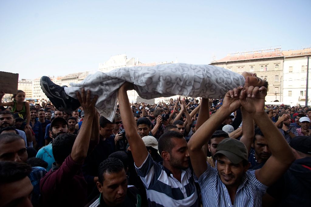 Budapest, 2015. szeptember 2. A budapesti Keleti pályaudvar elõtt várakozó illegális bevándorlók tiltakozásul egyik társukat emelik a fejük fölé 2015. szeptember 2-án. A rendõrség nem engedi õket felszállni a Németországba induló vonatra. MTI Fotó: Balogh Zoltán